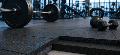 Modern gym with rubber flooring tiles, weightlifting equipment, and a layered floor cross-section showing gym flooring thickness.