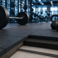 Modern gym with rubber flooring tiles, weightlifting equipment, and a layered floor cross-section showing gym flooring thickness.